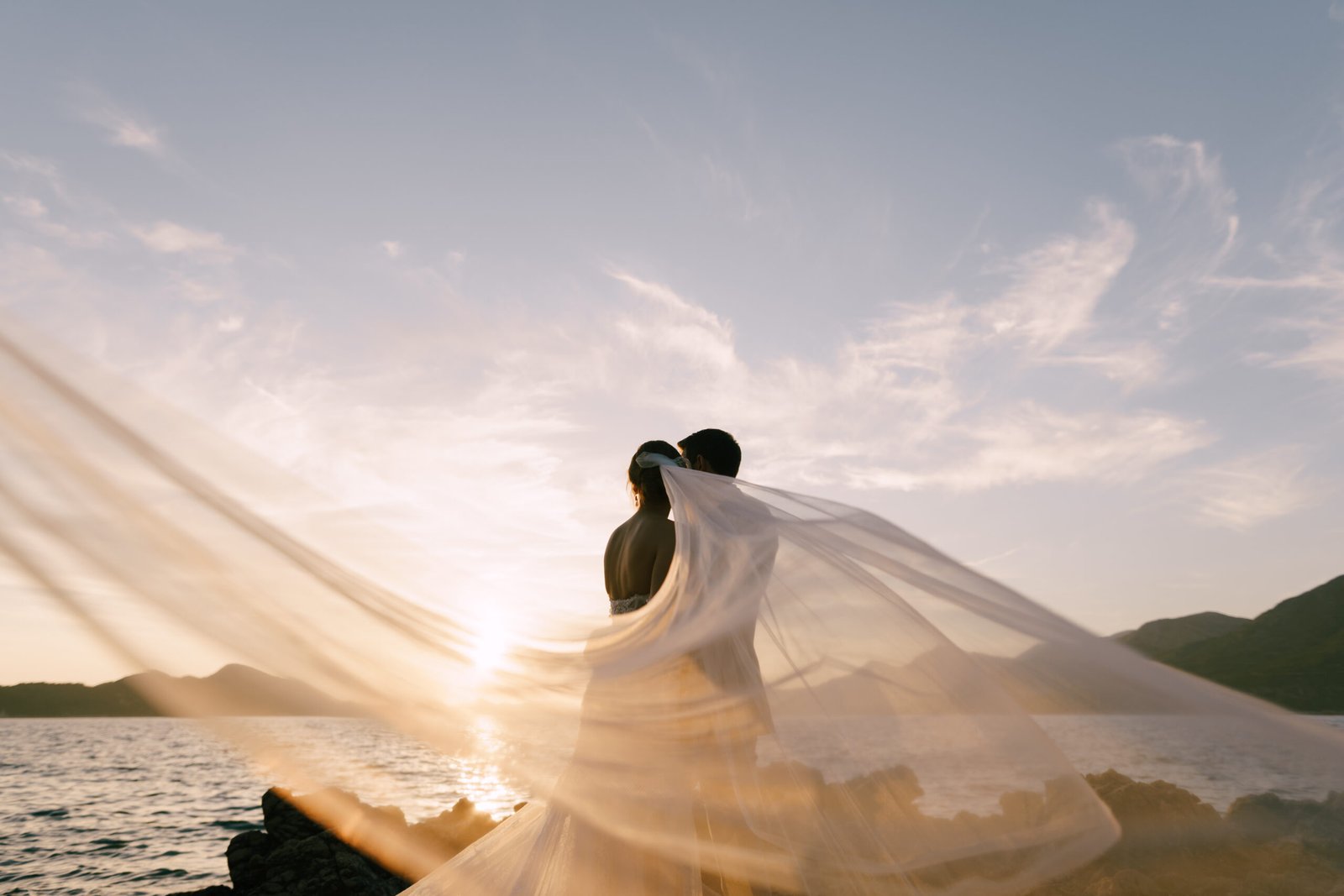 Groom holding bride with veil in the wind on a rocky Lake Superior shoreline