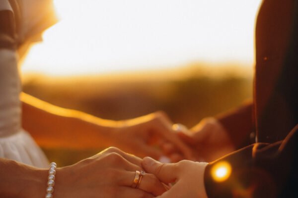 Couple holding hands with wedding rings at sunset